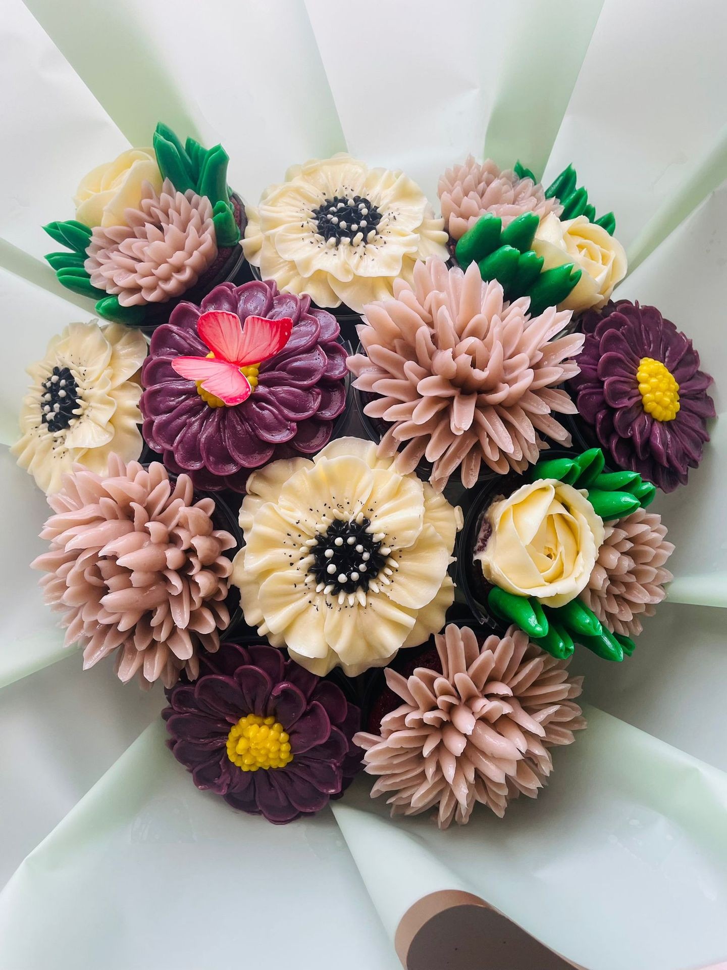 Beautiful arrangement of various colored buttercream flowers on a cake, with intricate details and green leaves.