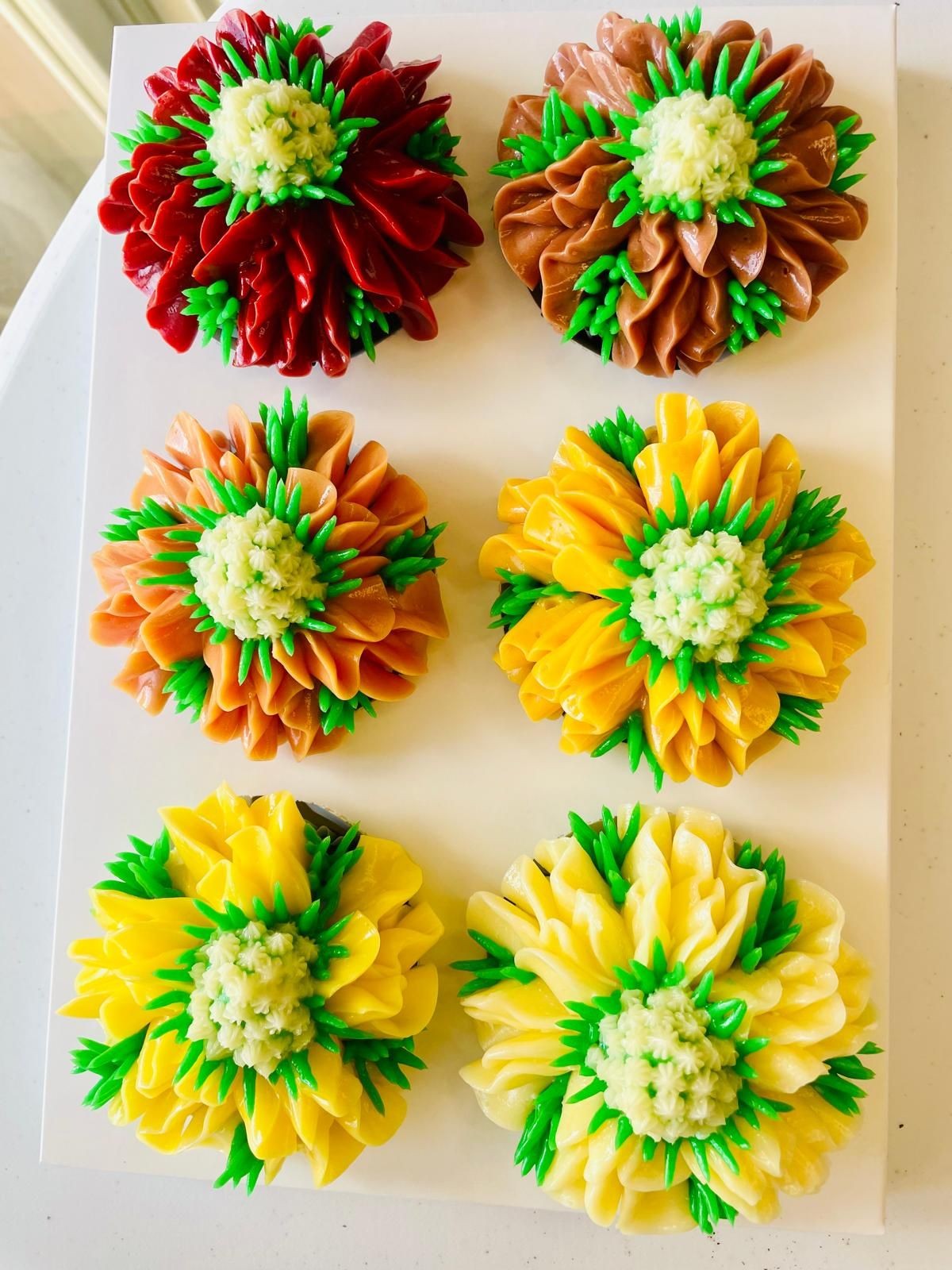 Assorted cupcakes decorated with colorful flower designs made of icing, displayed on a white surface.